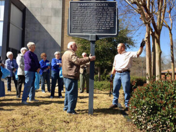 arborist informs a group of adults in pruning techniques near a Barbour County historical marker